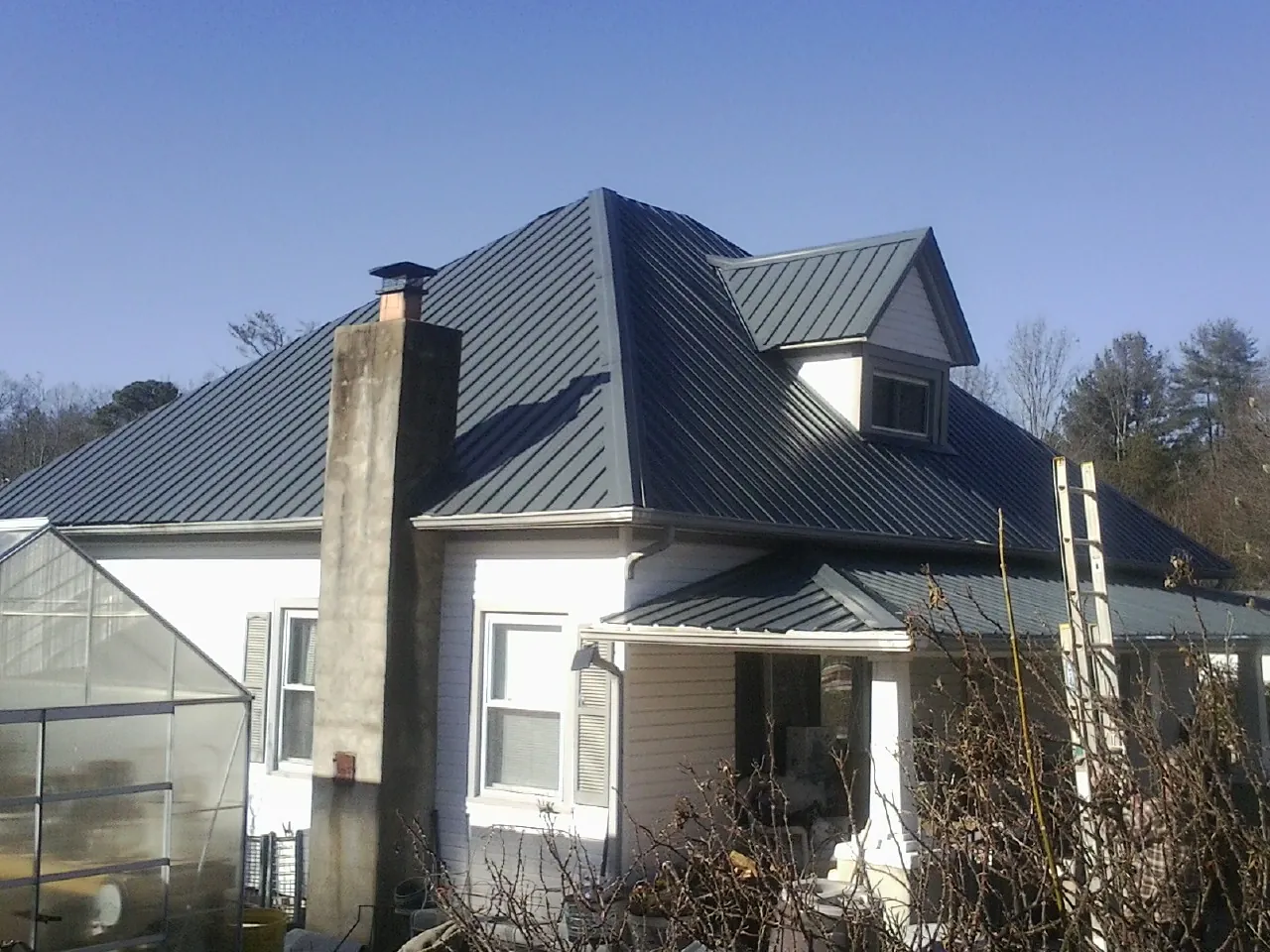 Dark blue standing seam metal roof on a white farmhouse with dormer — Slate & Tile Roof Repair by Roofing Brothers in Gunter