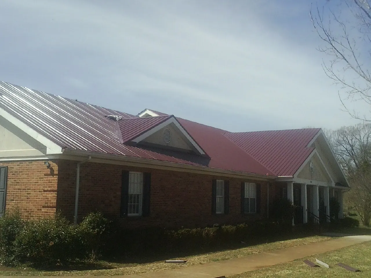 Red metal roof with gabled entries on a long brick building, from a Hail Damage Roof Repair job in Gunter