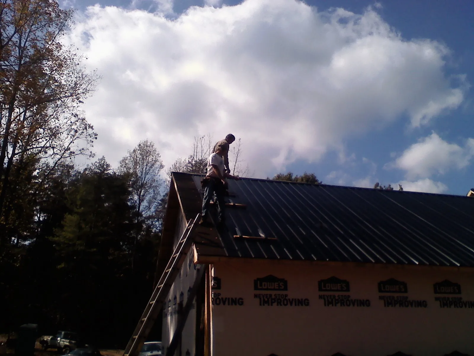 Roofer fastening dark metal panels high against a cloudy sky, from a Roof Inspection job in Gunter