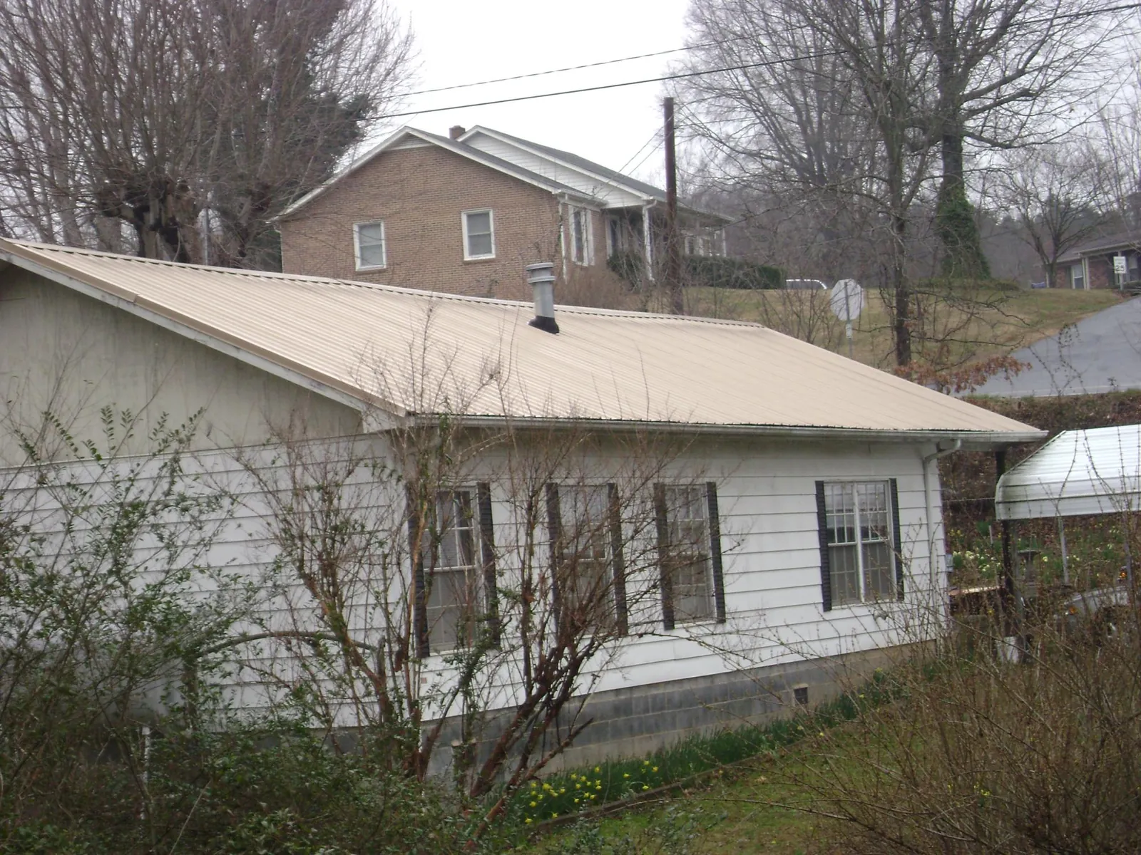 Tan metal roof on a white sided house set into a hillside — Commercial Roofing by Roofing Brothers in Gunter