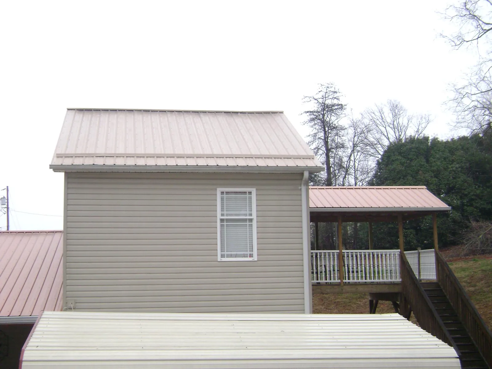 Tan metal roofs on a two story addition and attached porch, from a Roof Replacement job in Gunter